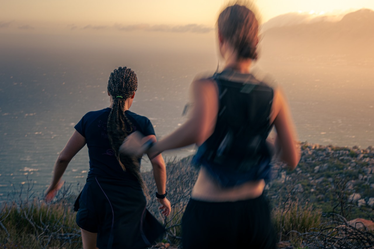 Two female trail runners in motion during golden hour with warm atmospheric lighting and mountain silhouettes