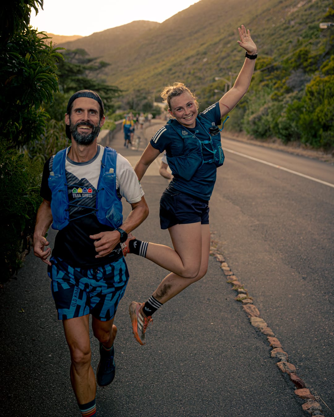 Two runners on paved road with female runner jumping in celebration during golden hour