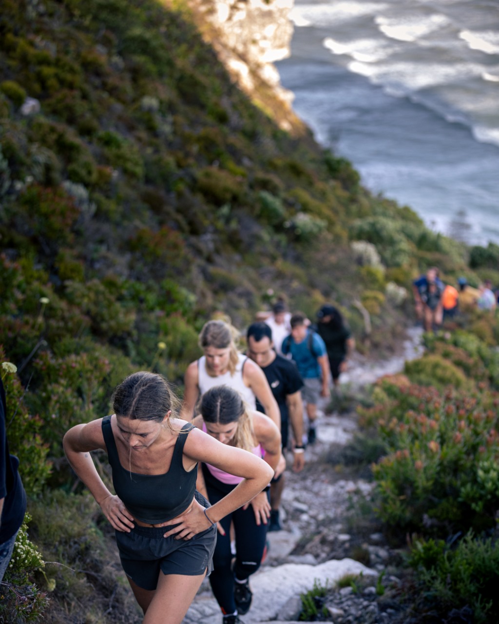 Trail runners navigating challenging rocky coastal path with ocean waves