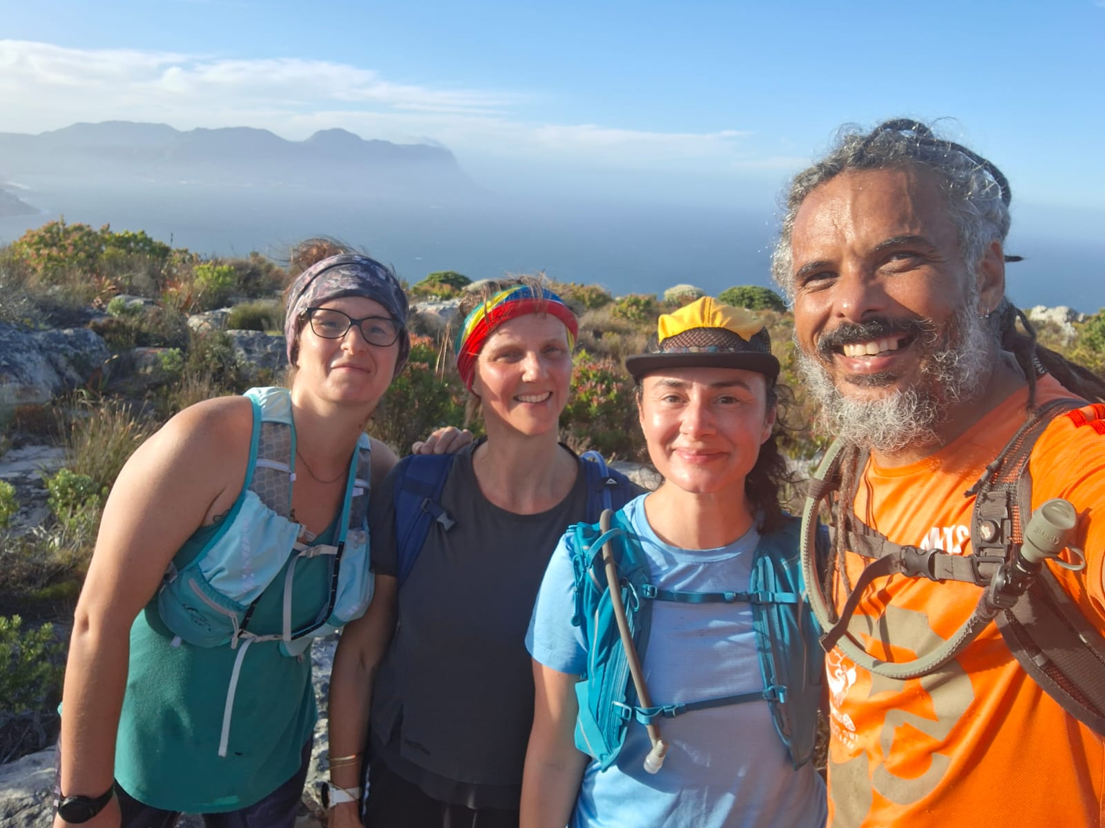 Group selfie of four TrailDawgs members on mountain with layered mountain ranges