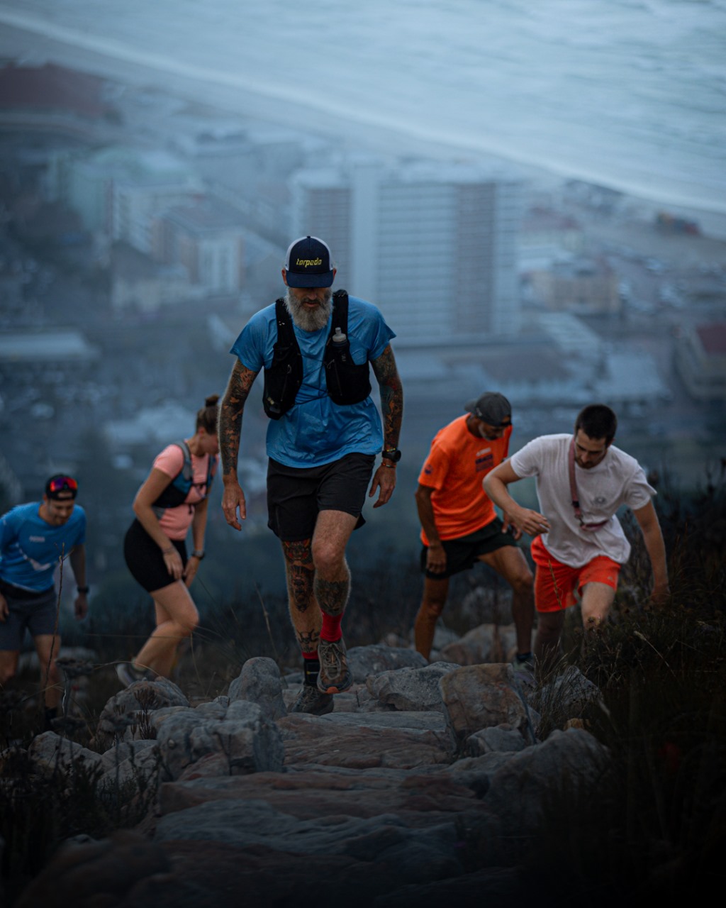 Group of trail runners navigating rocky terrain with city background