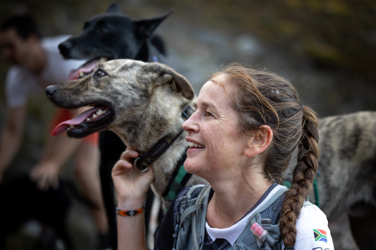 Female trail runner with braided hair smiling while petting happy dog