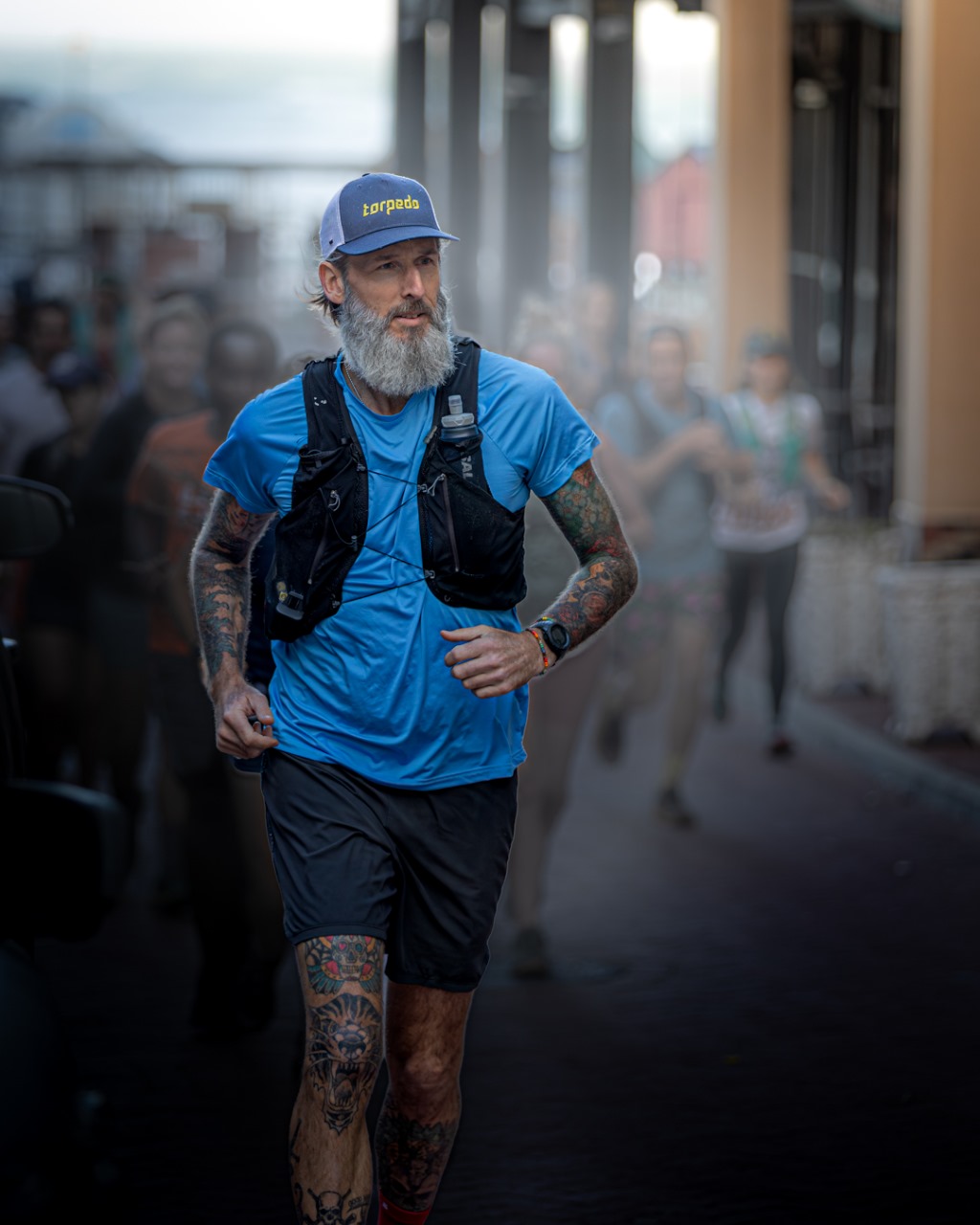 Bearded tattooed runner in blue shirt running through urban area